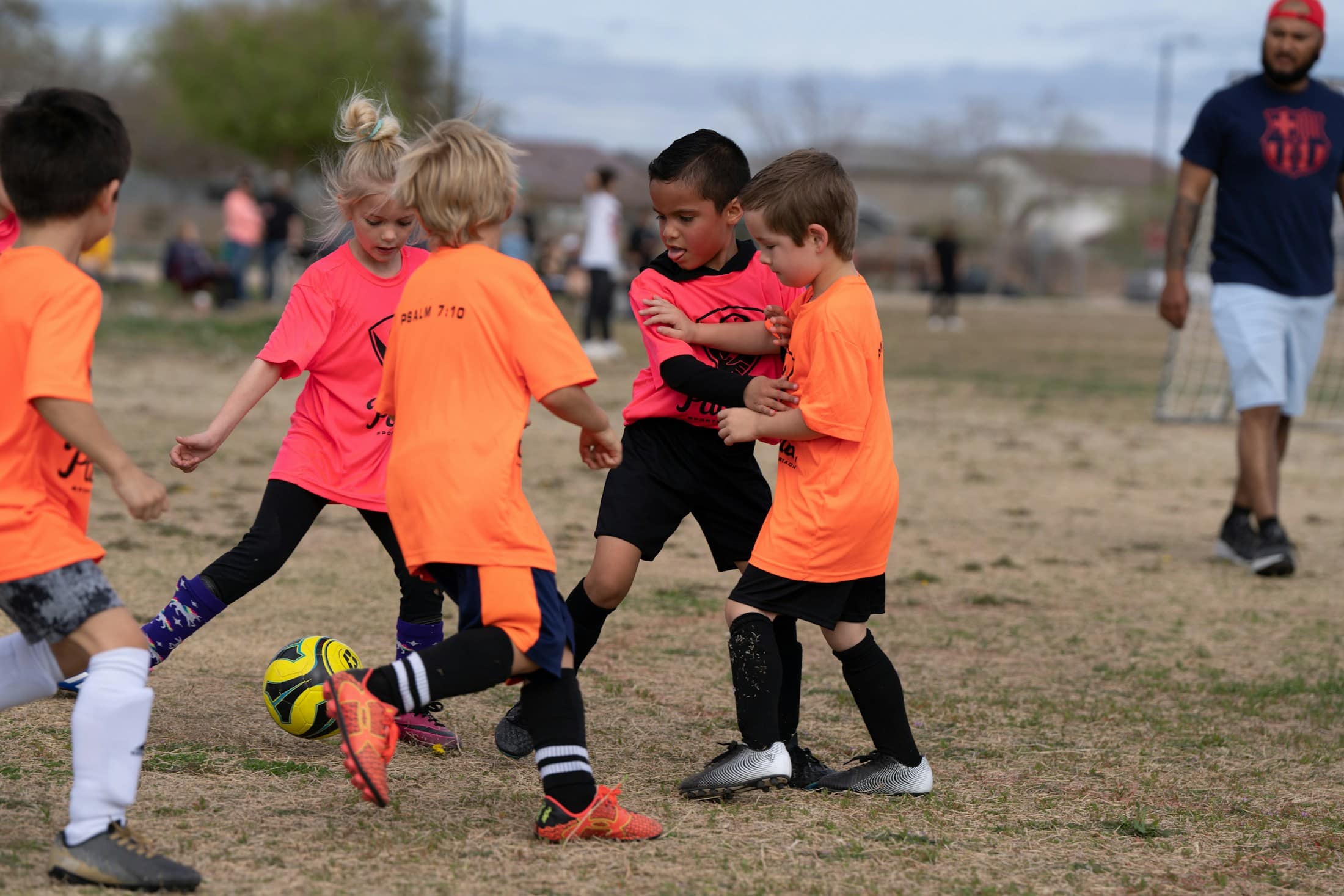 Kleine Kinder in orangenen und schwarzen Trikots laufen gemeinsam einem Ball hinterher