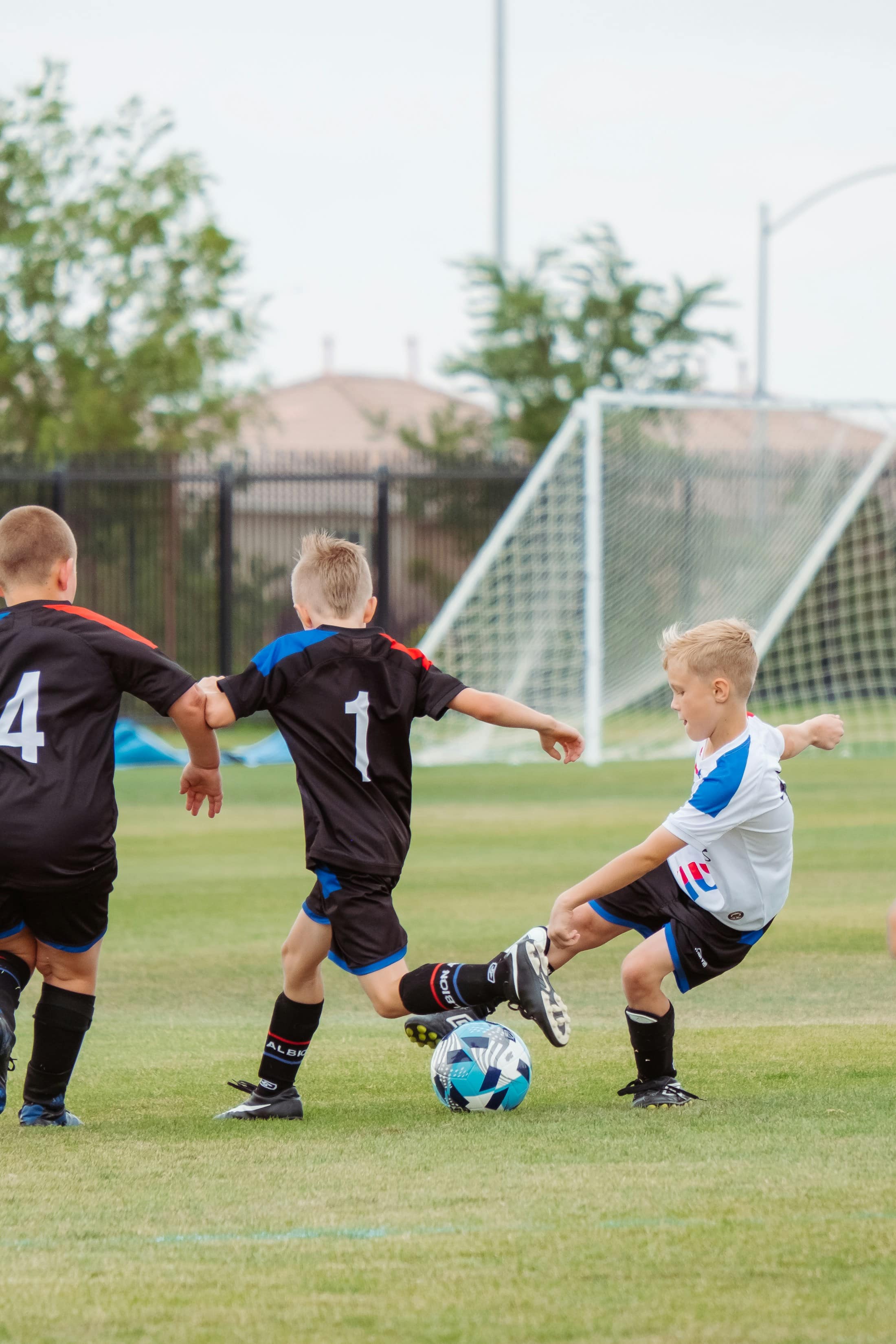 Drei Jungen laufen im Spiel einem Ball hinterher, einer holt zum Schuss aus