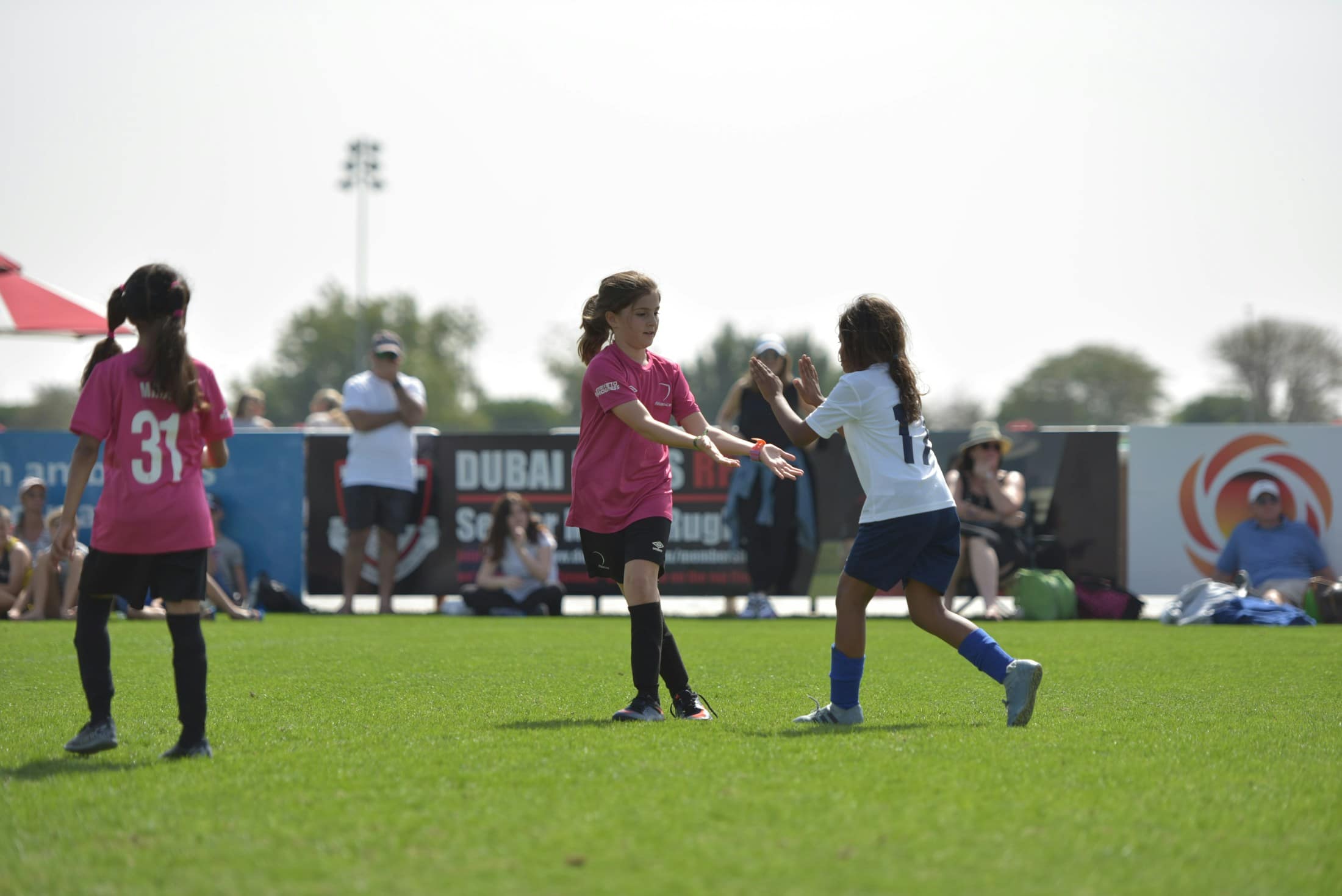 Mädchen in pinken und weißen Trikots spielen auf einem Rasenplatz Fußball