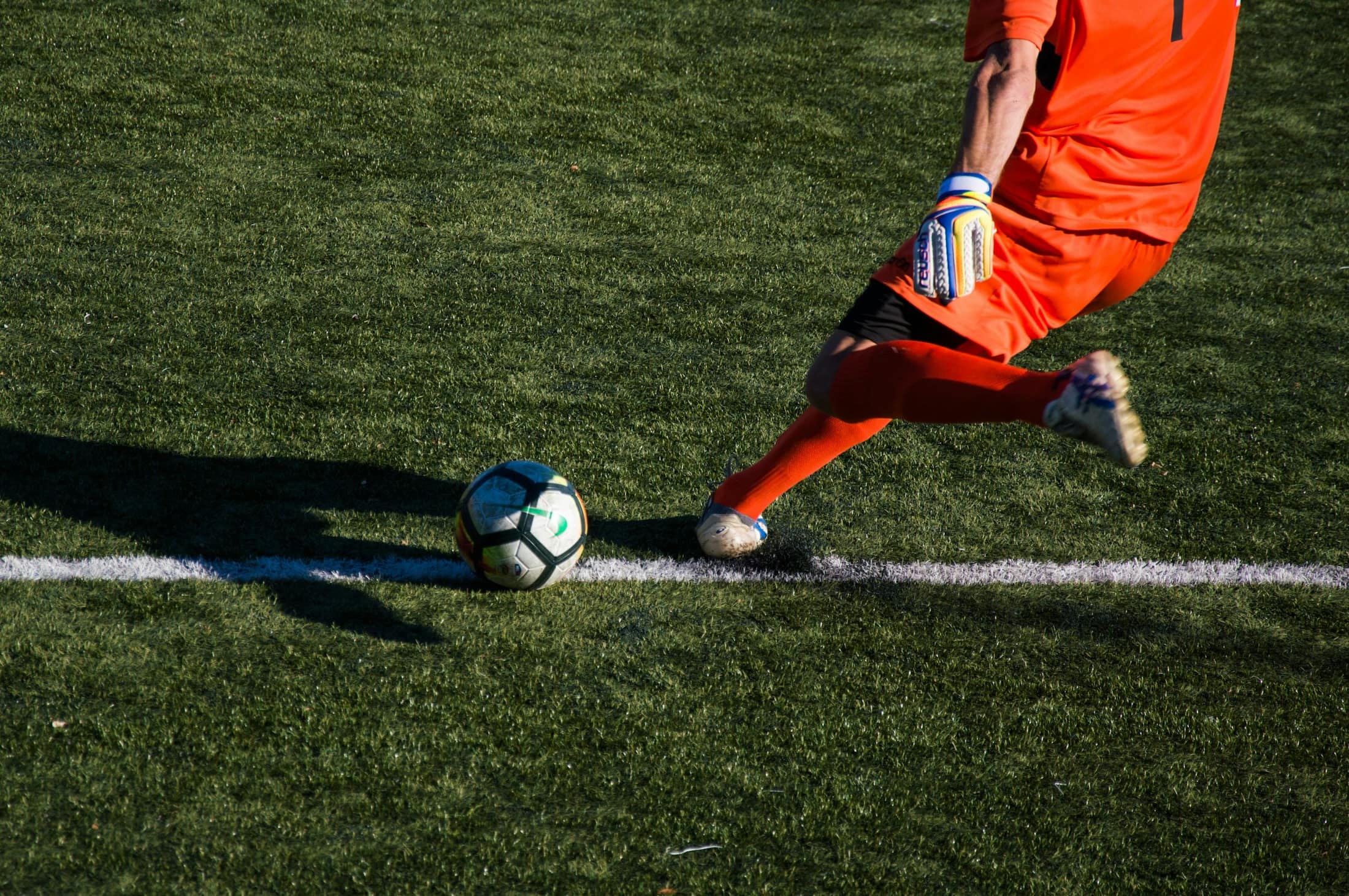 Spieler in orangem Trikot holt an der Seitenlinie zum Schuss aus