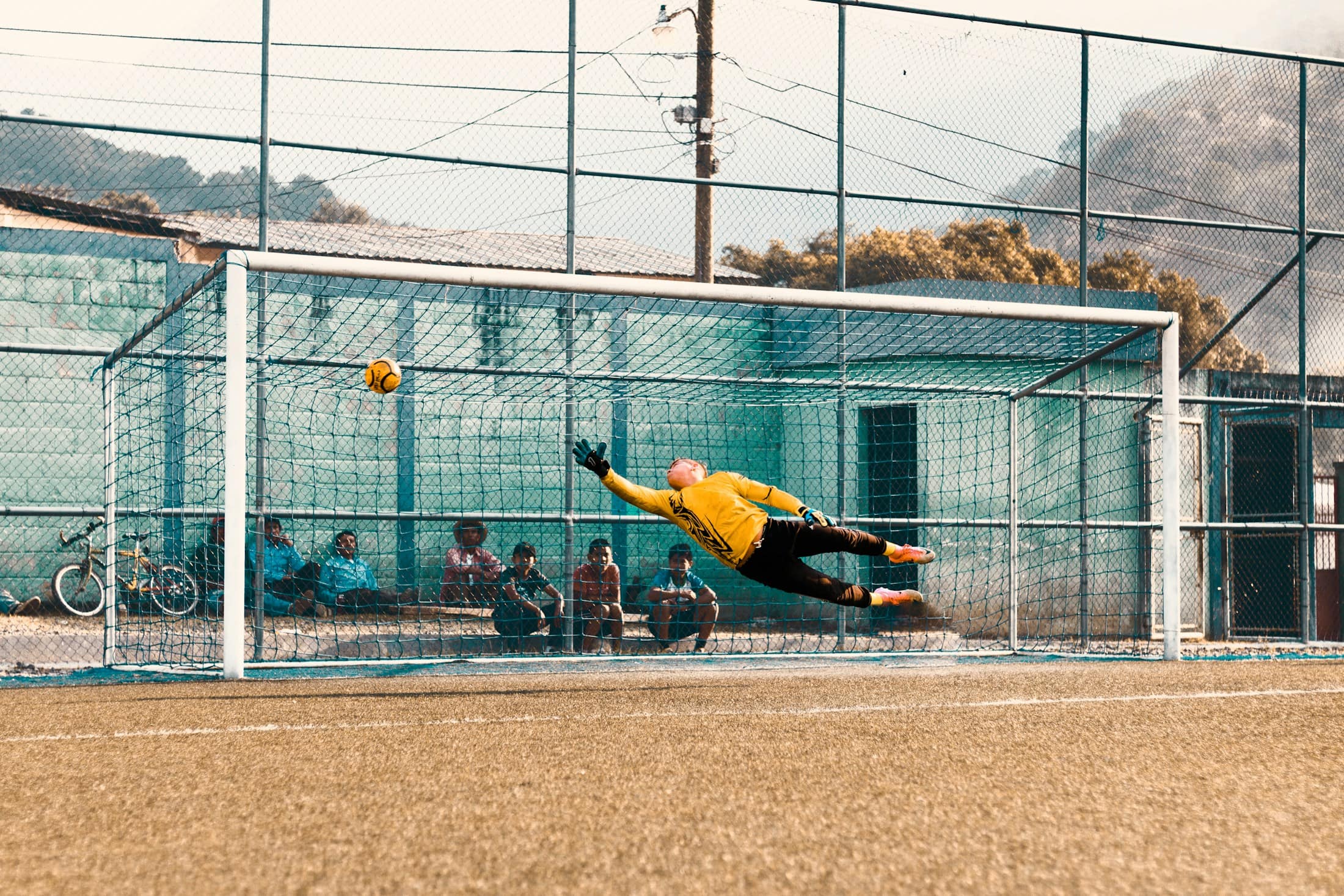 Ein Torwart in gelbem Trikot fliegt waagerecht durch die Luft und lenkt den Ball am Tor vorbei